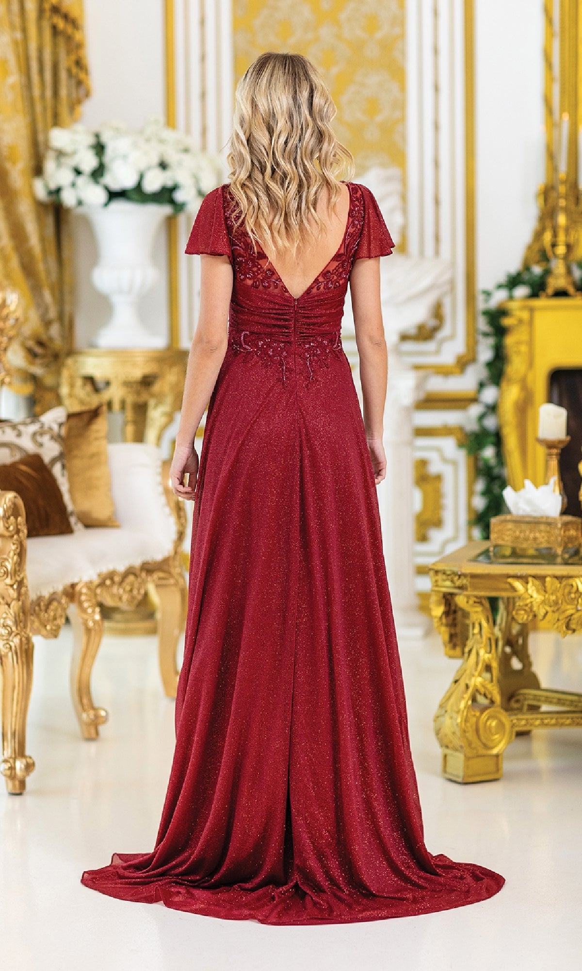 A woman wears the Dancing Queen 4496 short-sleeve long formal dress, facing away in an ornate room with white and gold decor.
